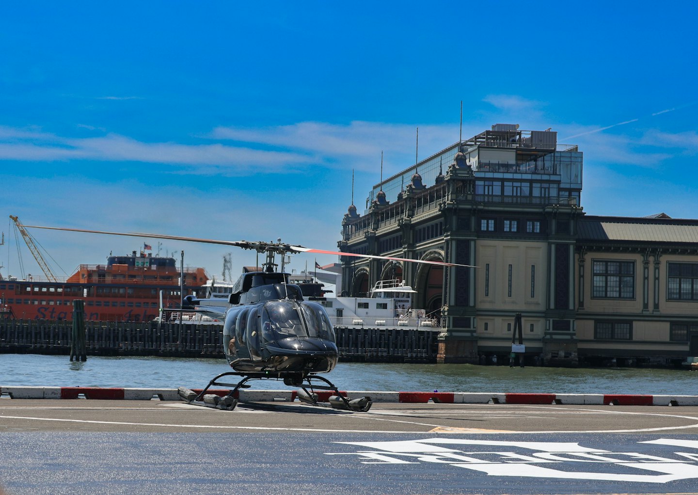A black helicopter parked on a helipad beside a historic waterfront building.