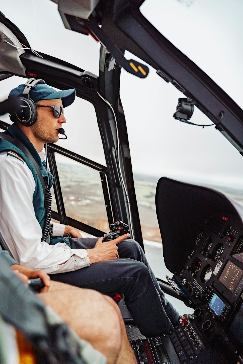 Pilot in uniform sits in helicopter cockpit holding controls.
