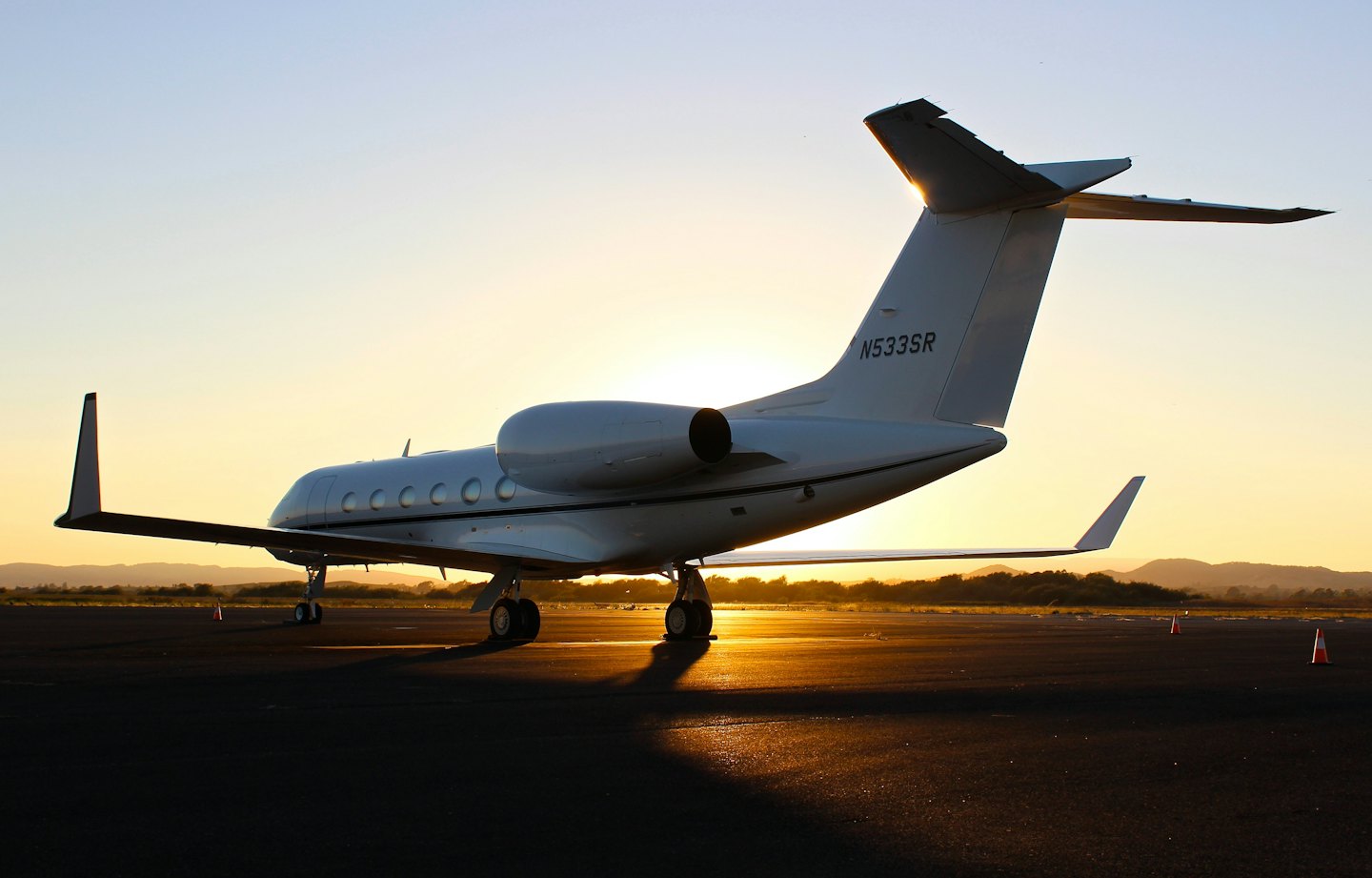 A white private jet sits on an asphalt runway at sunset.