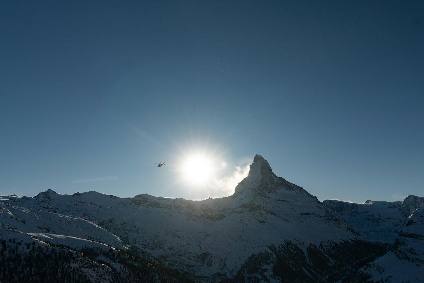 Small helicopter flying over a snow-covered mountain peak.