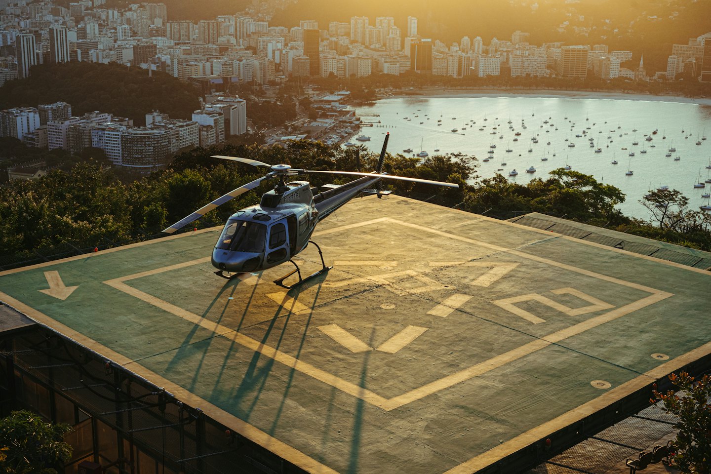 A grey helicopter parked on a city helipad overlooking the bay.