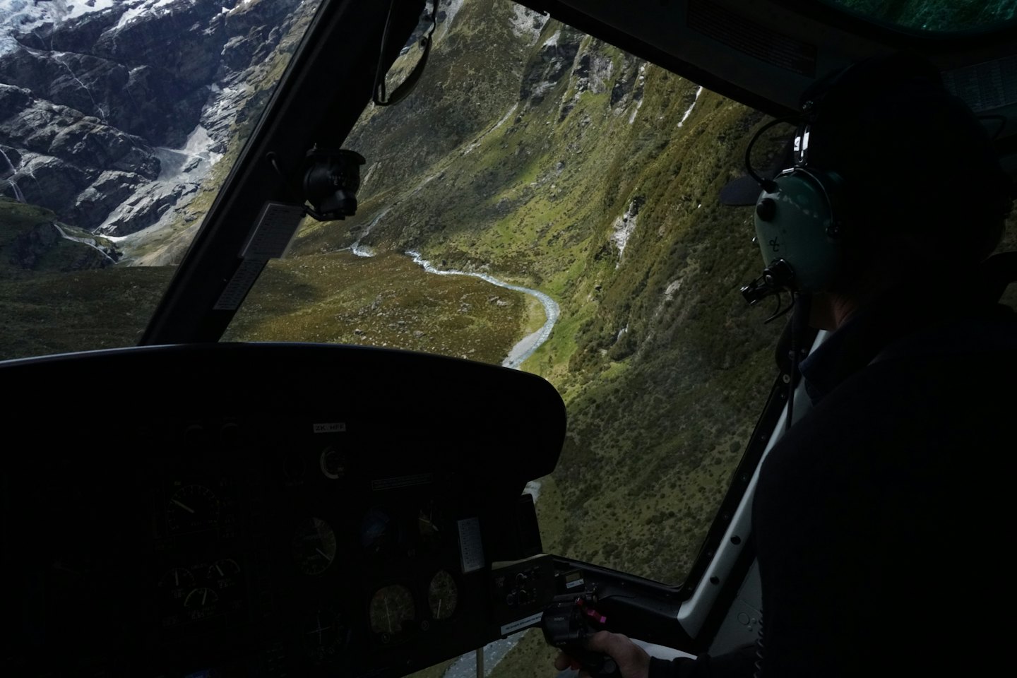 Pilot in headset flies helicopter over green mountain valley.