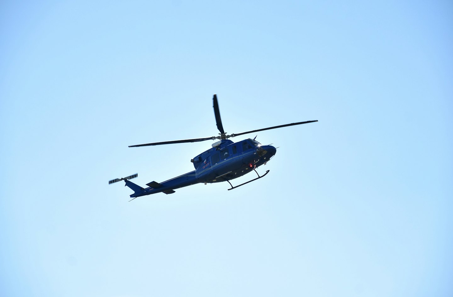 Dark blue helicopter flies through a clear blue sky.