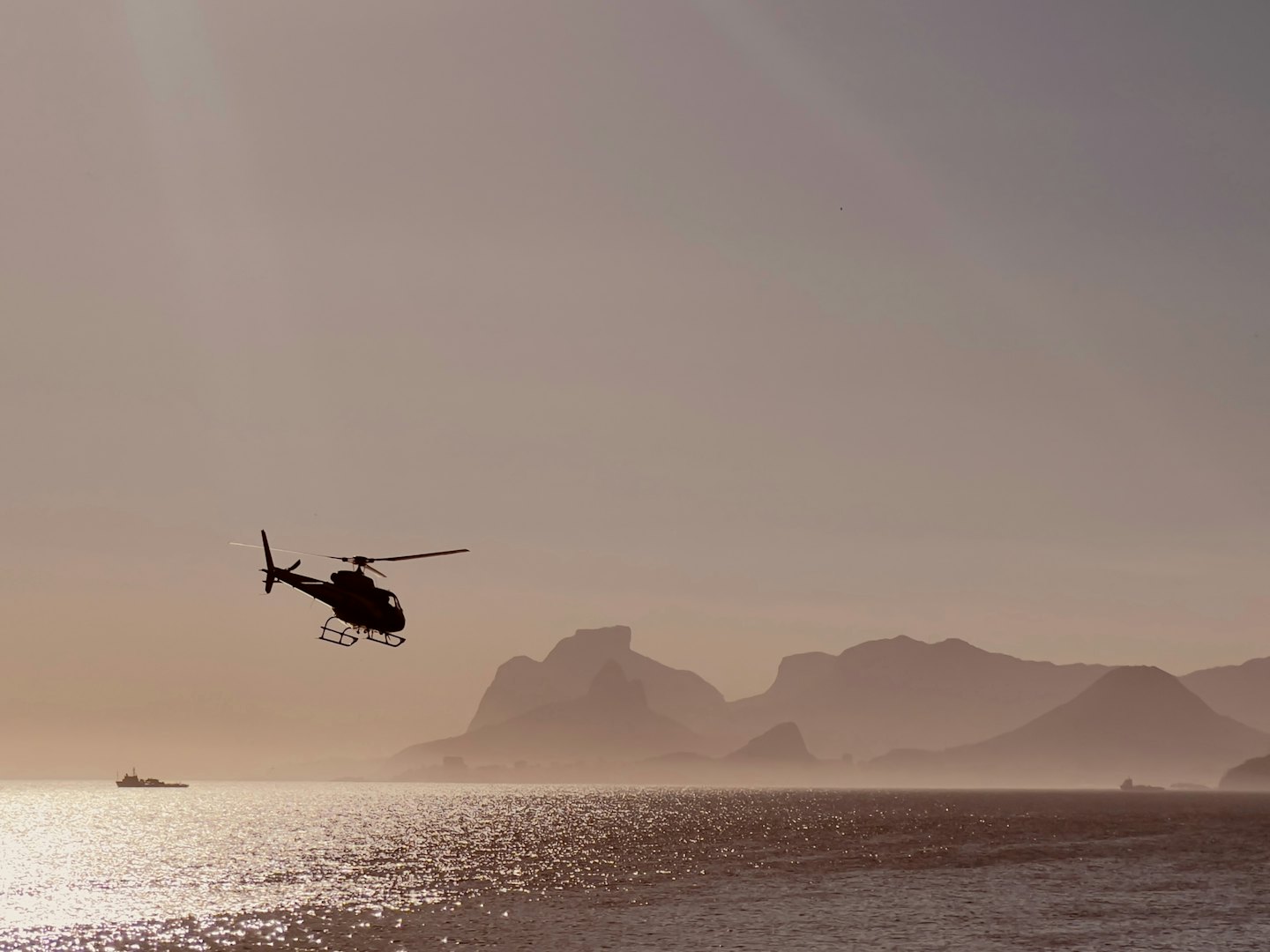 A helicopter flies above a boat on the water.